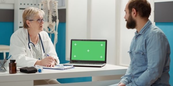 Senior doctor and patient looking at laptop with greenscreen